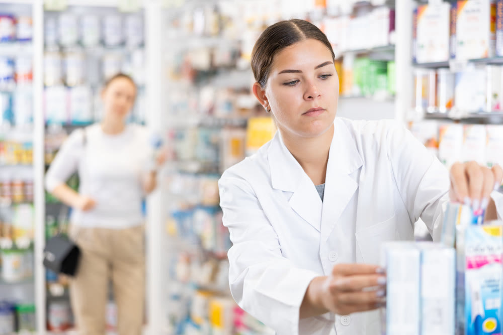 In pharmacy, woman chemist makes out showcase with warming analgesic ointments