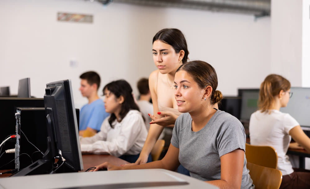 Portrait of young female student helping her female friend studying in computer class using pc in library