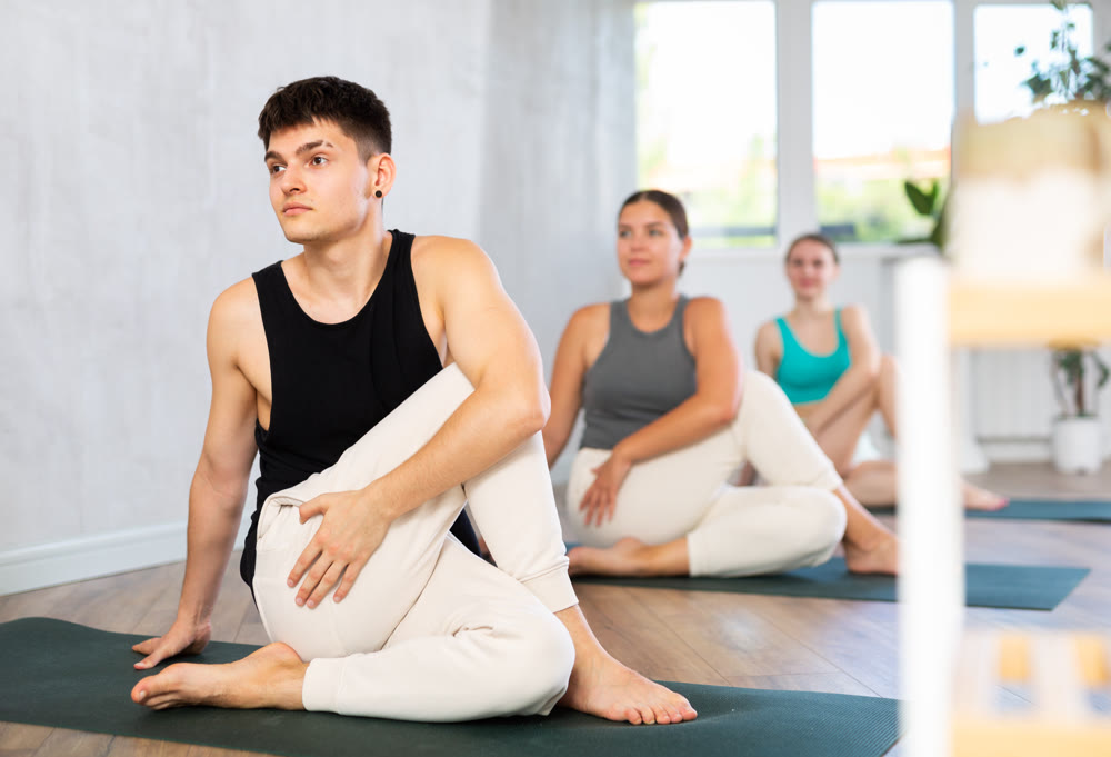 Woman and man performing Ardha Matsyendrasana position during group yoga training in fitness gym