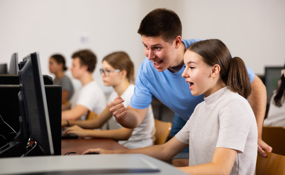 Positive young student emotionally reacting while working at pc in computer class