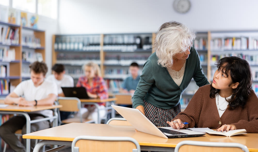 Mature woman teacher cheks the assignment from a schoolgirl