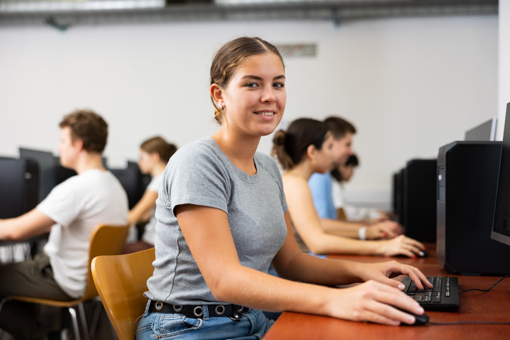 Smiling female student using PC and studying computer science in the classroom