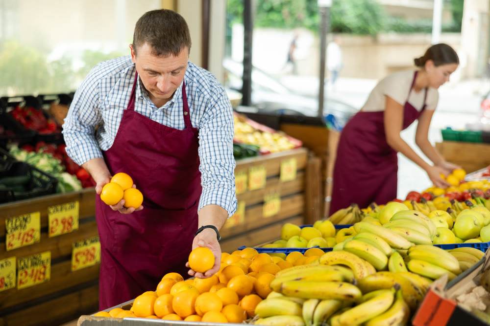 Male seller working in supermarket and lays out oranges on counter