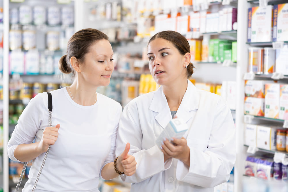 In cosmetic department of pharmacy, surprised woman listens to pharmacists story about new cream
