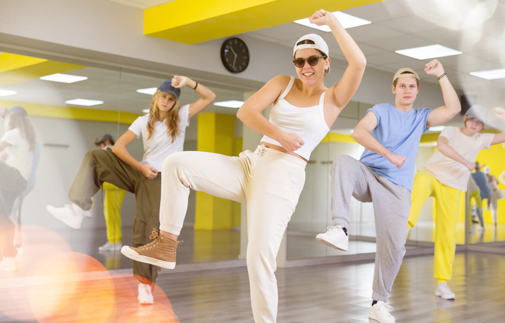 Expressive young people practicing new movement in dance with leg out to side in dance room