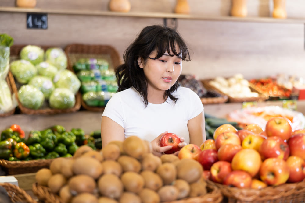 Young asian girl choosing ripe apples on store display