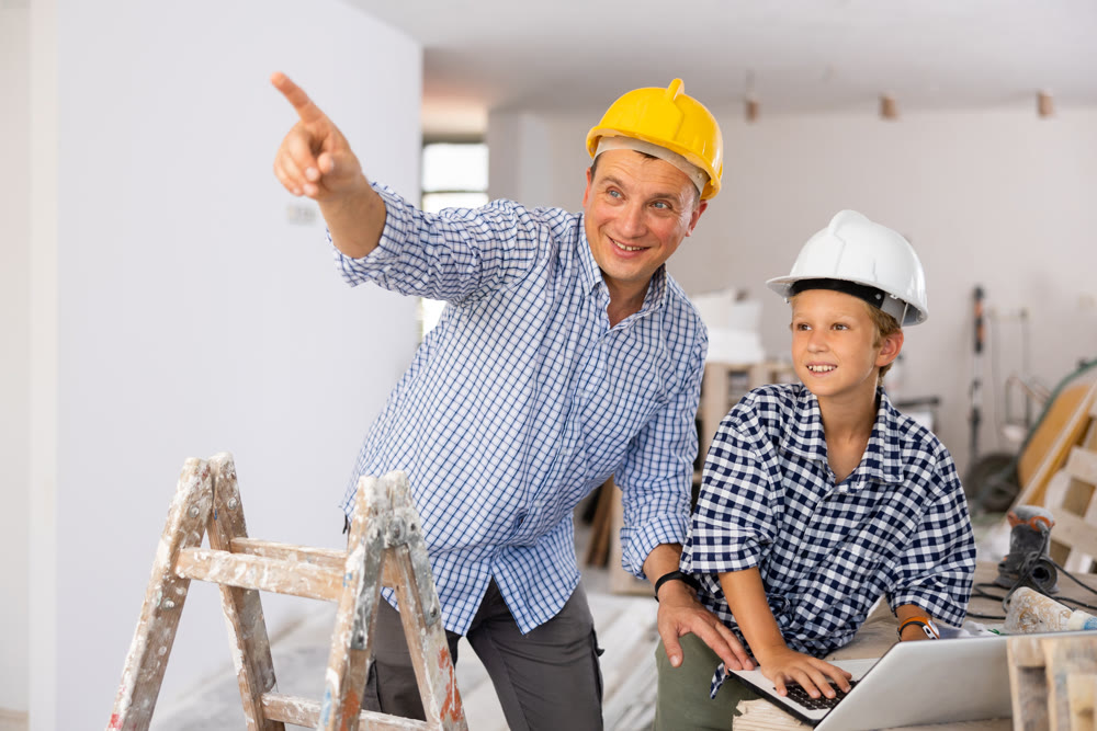 Man architect and boy using laptop while discussing working process in house being renovated