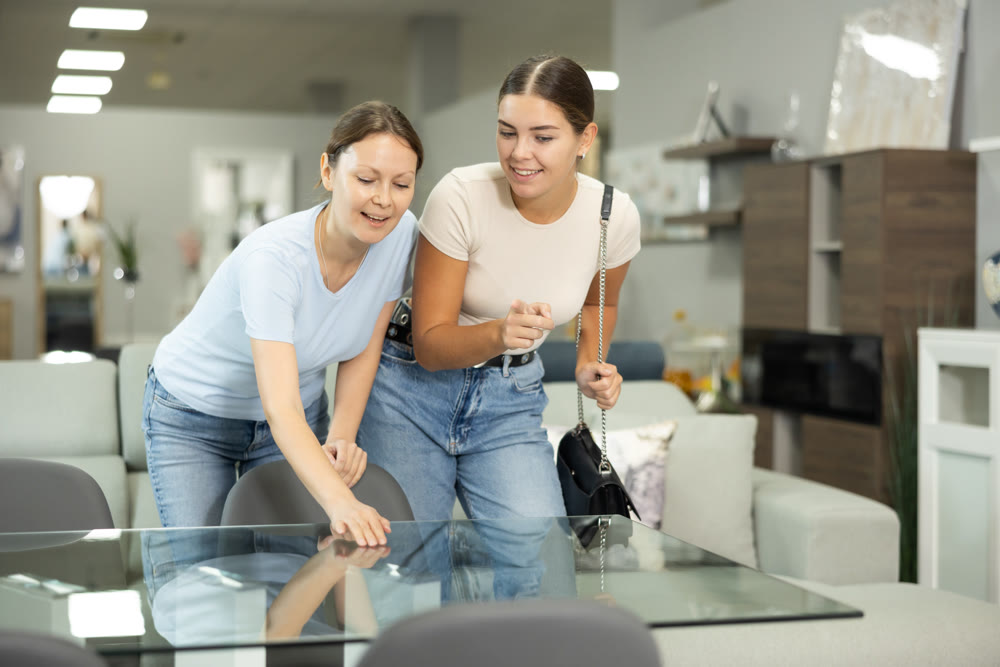 Positive young women choosing dining table in furniture store