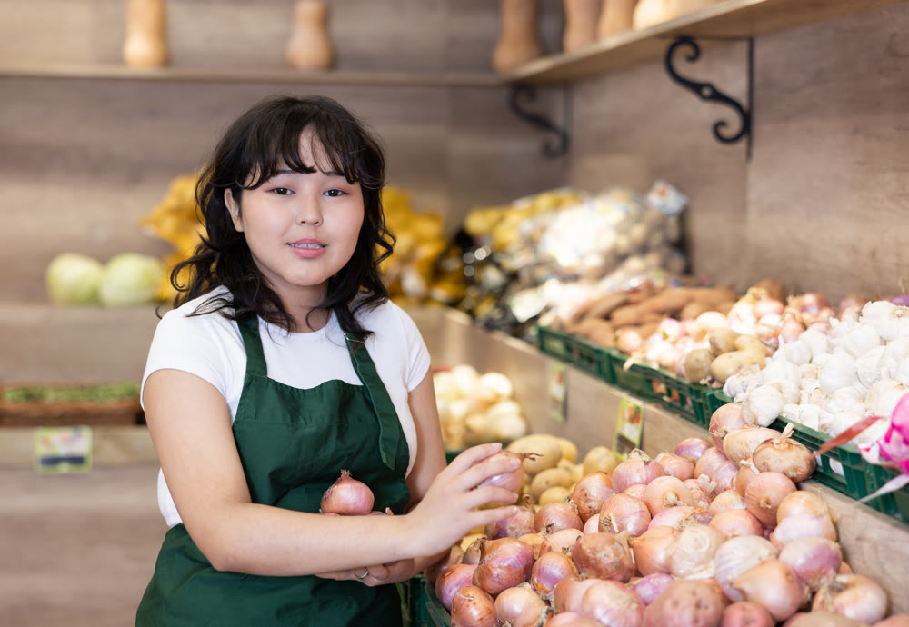 Young salesgirl at her first job, selling onions in vegetable shop
