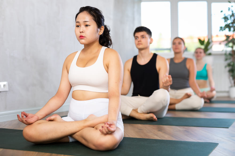 Group of young people meditating in a lotus pose.