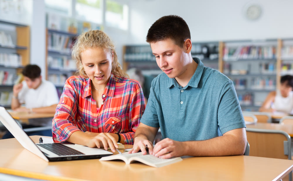 European schoolgirl with a classmate in the library is preparing for lessons