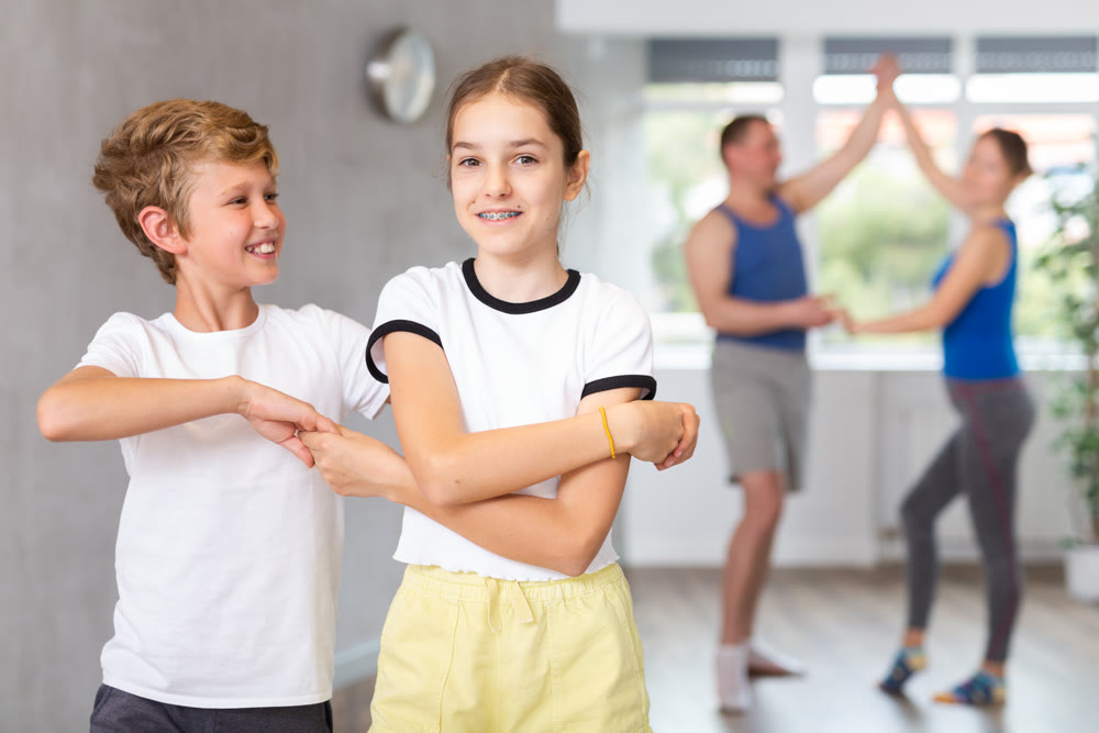 Happy preteen boy and girl practicing dance in pairs together with their parents