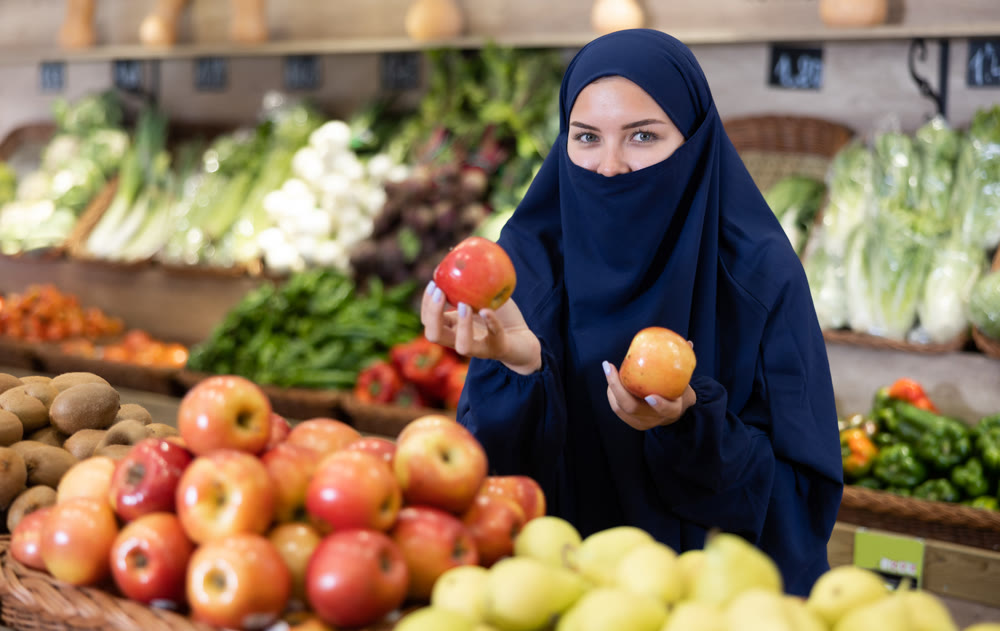 Delighted young Muslim woman purchaser choosing apples in grocery store