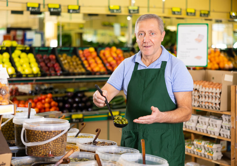 Elderly salesman showing olives in grocery store