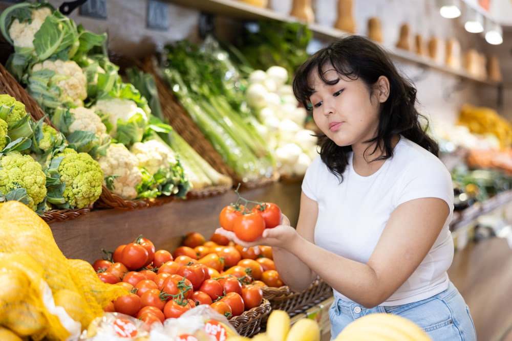 Young asian girl selecting ripe red tomatoes in supermarket