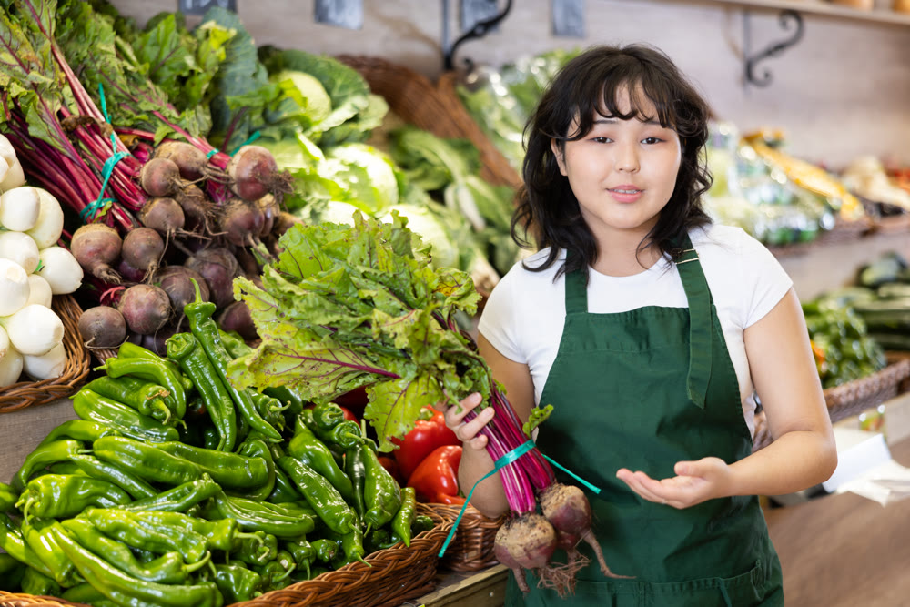 Young asian salesgirl offering fresh beets in greengrocery