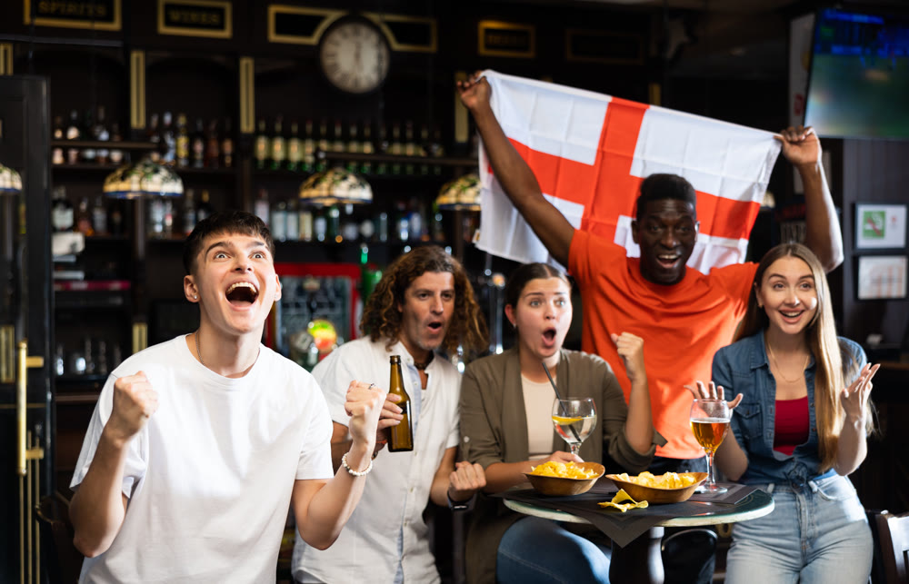 Cheerful multiracial soccer fans waving the flag of England and watching tournament in sport bar