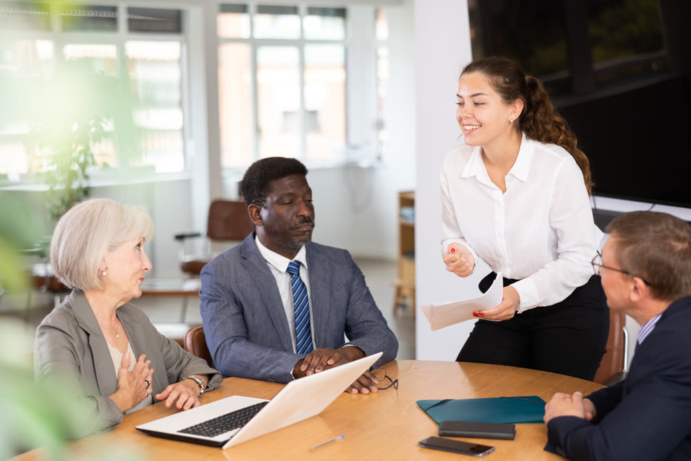 Young woman head of department speaks at meeting ahead frowning colleagues