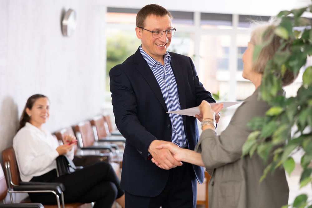 Middle-aged man handshaking with other person in waiting room