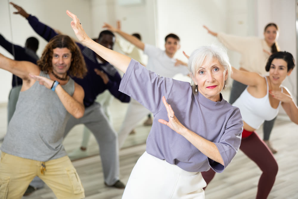 Elderly woman practicing modern vigorous dance movements with group