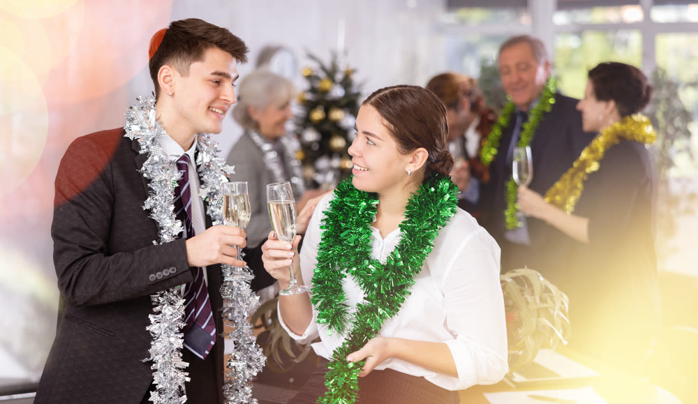 Two joyful male and female coworkers with tinsels and glasses of champagne during corporate New Year party in office