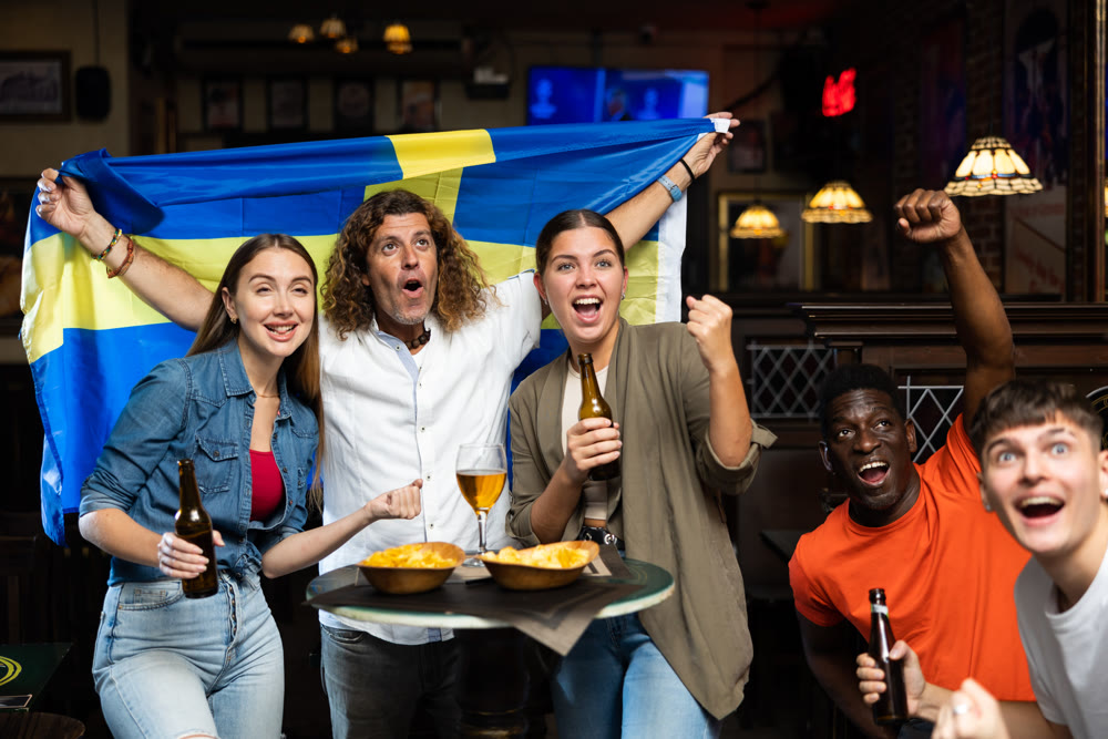 Cheerful people cheering for favorite Swedish sports team in pub