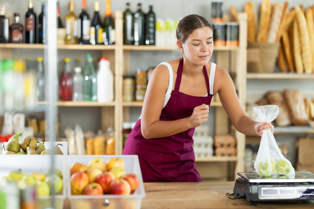 Young woman seller weighs apples in bag