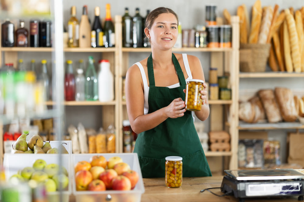 Young woman seller offering olives in grocery store
