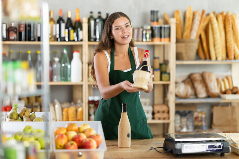 Young female seller offering wine in grocery store