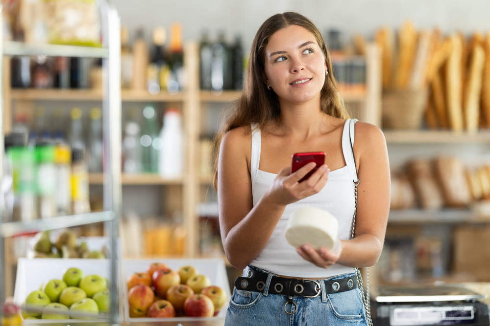 Female shopper scans QR code on cheese label using smartphone. Checking products in supermarket