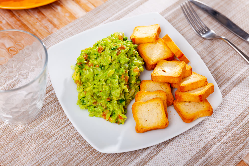 Delicious bowl of guacamole on table with toasted bread