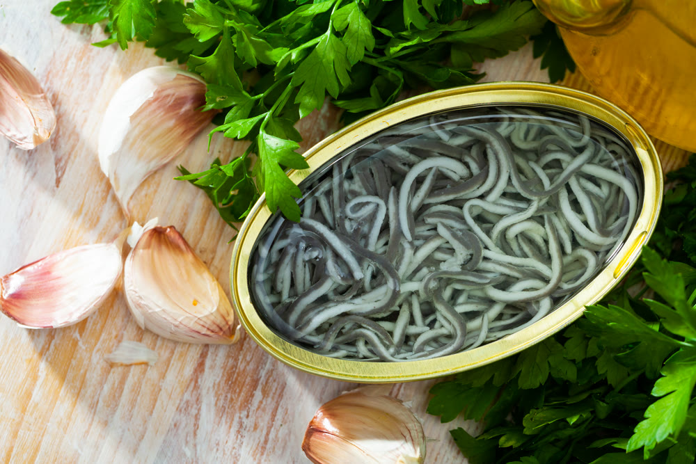 Pickled eels in open tin can with garlic at table