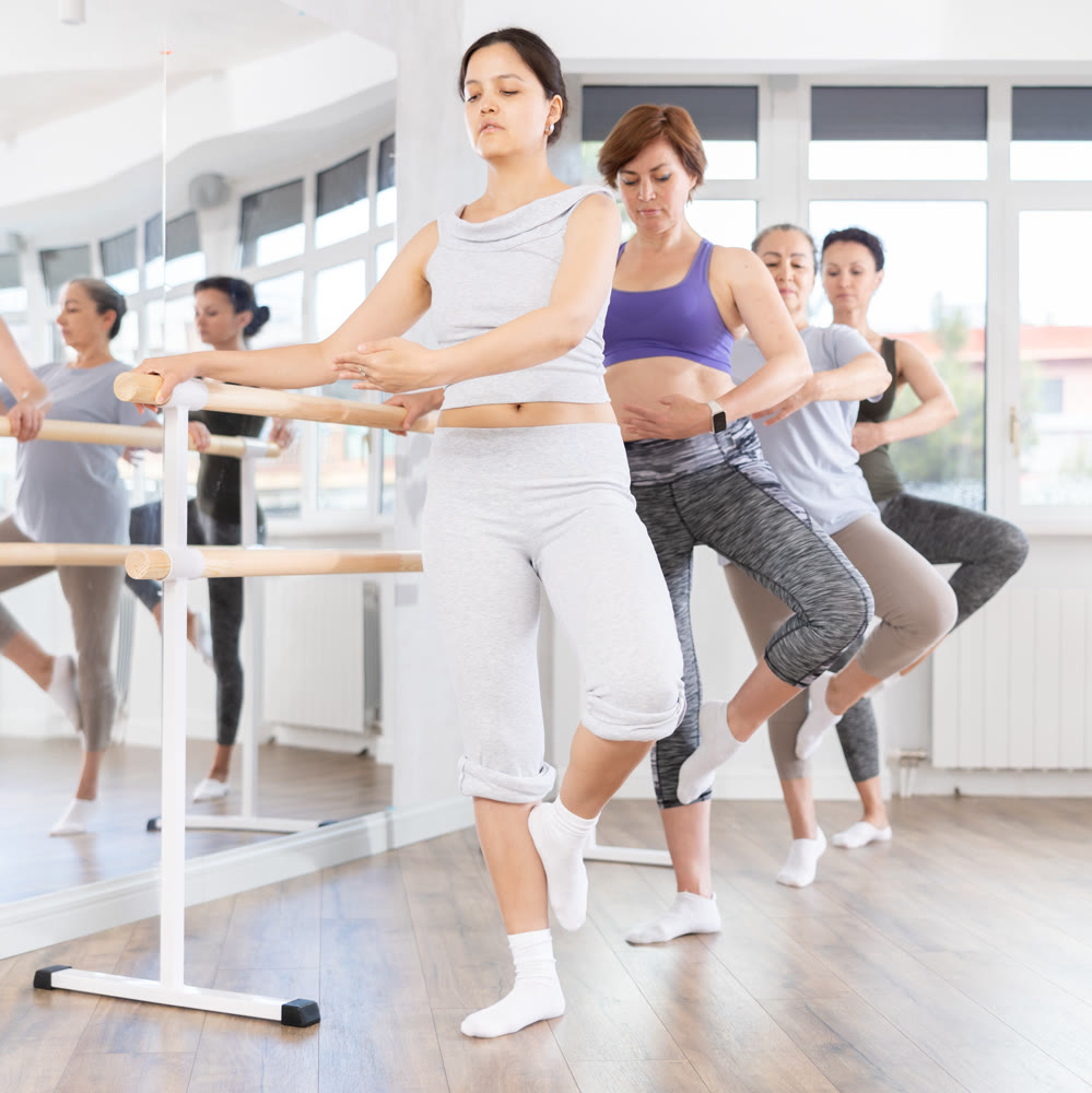 Group of female beginners performing fondue at barre