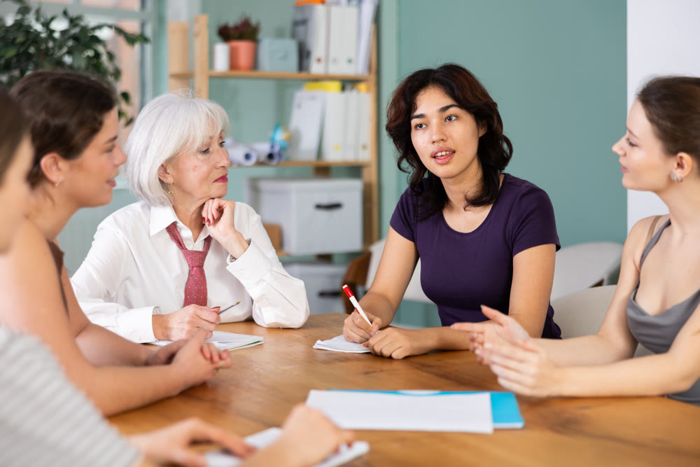 Interested office female workers sitting at table with papers and discussing ideas during business meeting in office