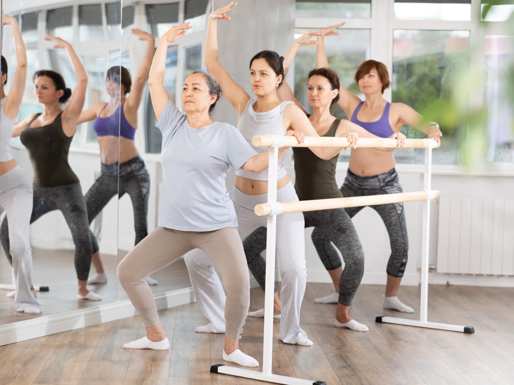 Women doing ballet at group amateurs training session in the studio performs demi plie near the ballet barre, standing in ballet stance