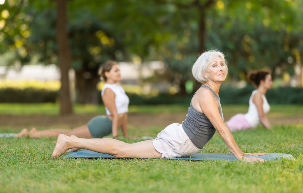 Senior woman doing Upward Facing Dog pose during group yoga in park